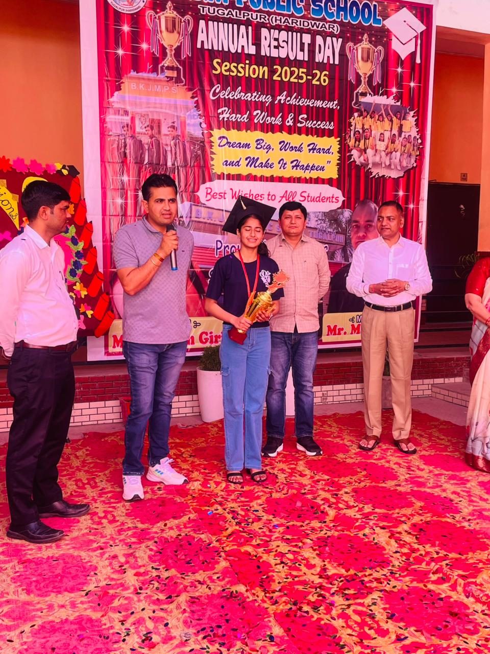 A student topper speaking on stage with the trophy